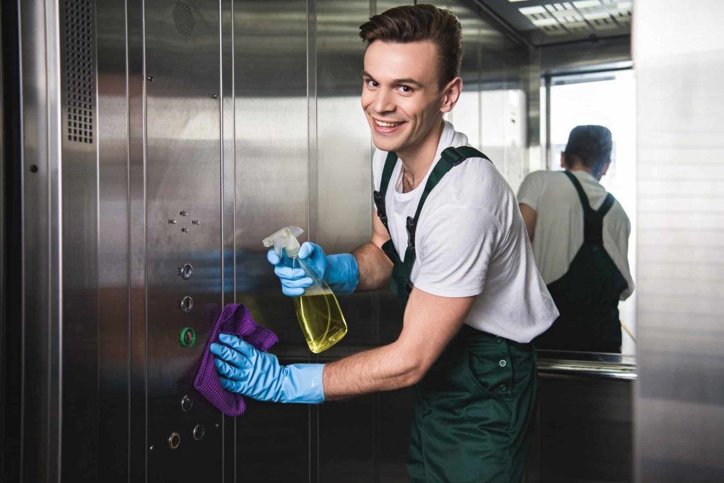 Bărbat curățând lift cu soluție și mănuși albastre.