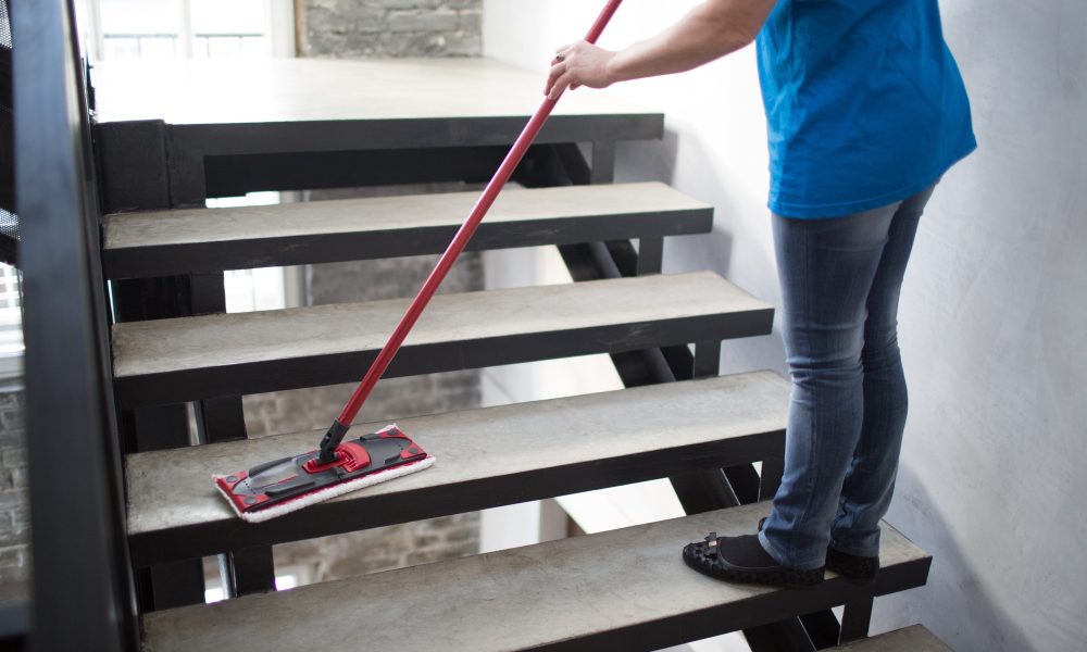 Curățare scări cu mopul roșu de către femeie.