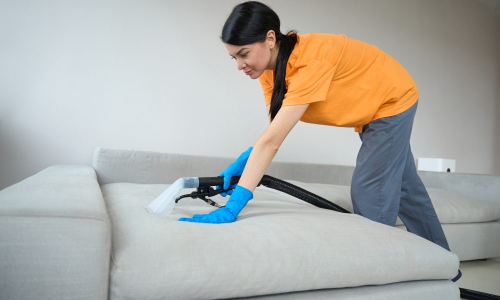 Femeie curăță canapea cu aspirator special.