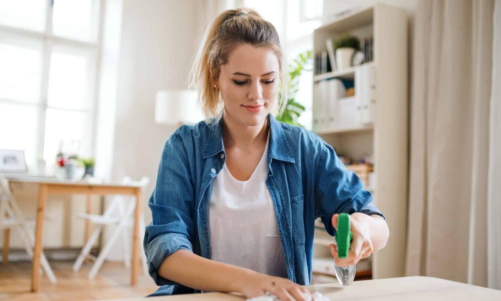 Femeie curăță masă în sufragerie luminoasă.